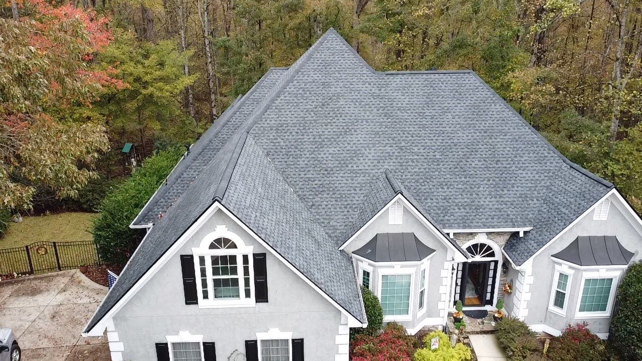Gray house with a dark gray shingle roof surrounded by trees with autumn foliage.