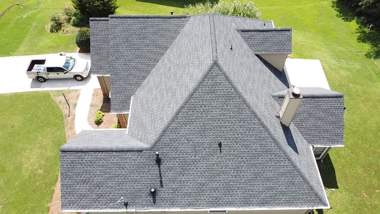 Overhead view of a house with gray shingle roof, chimney, and a white truck parked nearby on a grassy lawn.