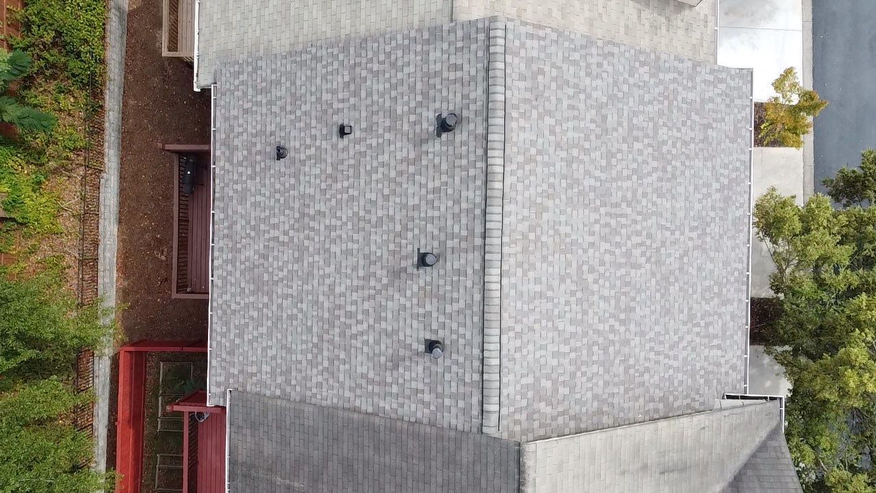 Overhead view of a building with a textured gray exterior, black hardware, and a small tree beside it.