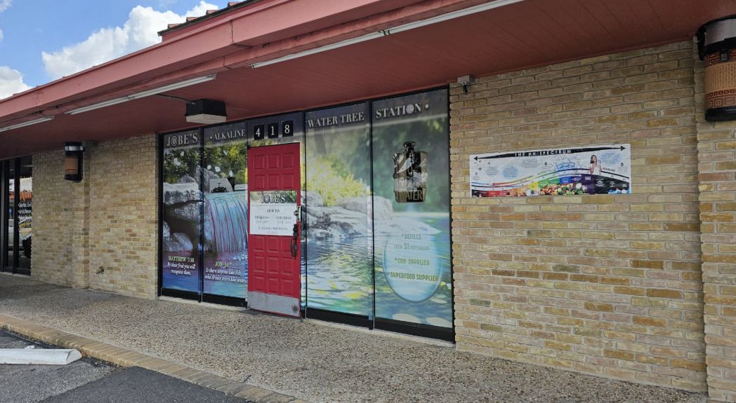 Exterior of a business with large window displays, red awning, and beige brick facade.