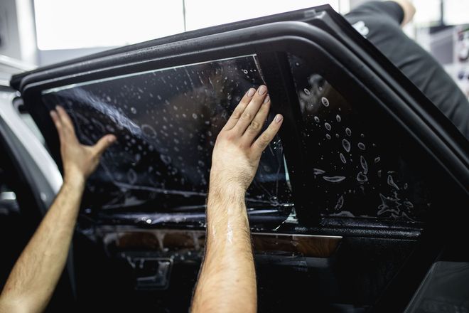 A professional installs automotive window tint, applying a wet film sheet to the inside of a car window.
