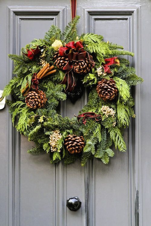 A christmas wreath is hanging on a gray door.