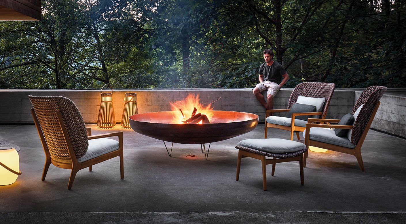 A man is sitting at a fire pit surrounded by chairs.