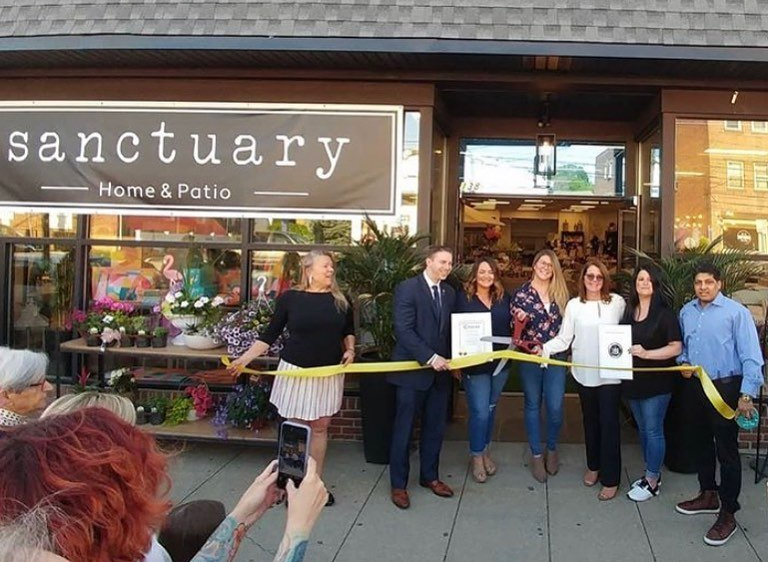 A group of people are cutting a yellow ribbon in front of a store called sanctuary