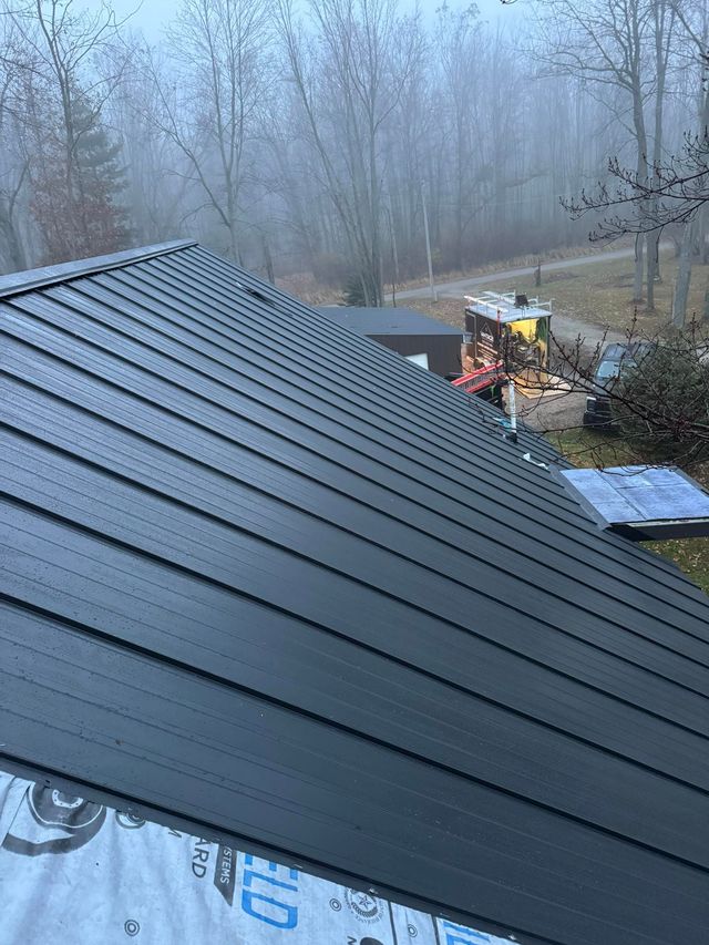 Dark metal roof under construction with workers and equipment on a foggy hillside