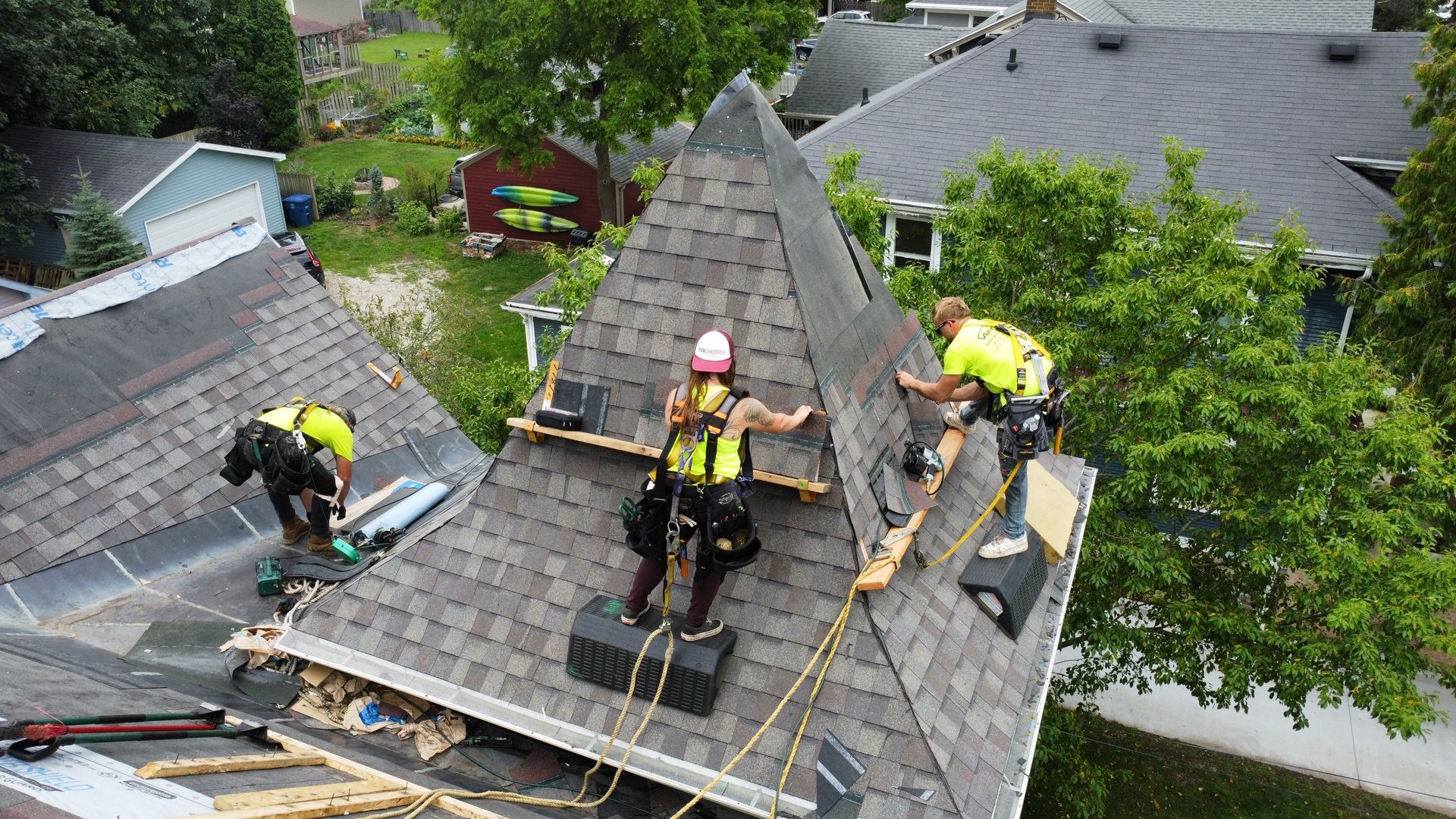 Roofing workers repairing a steep shingled roof with safety harnesses and tools