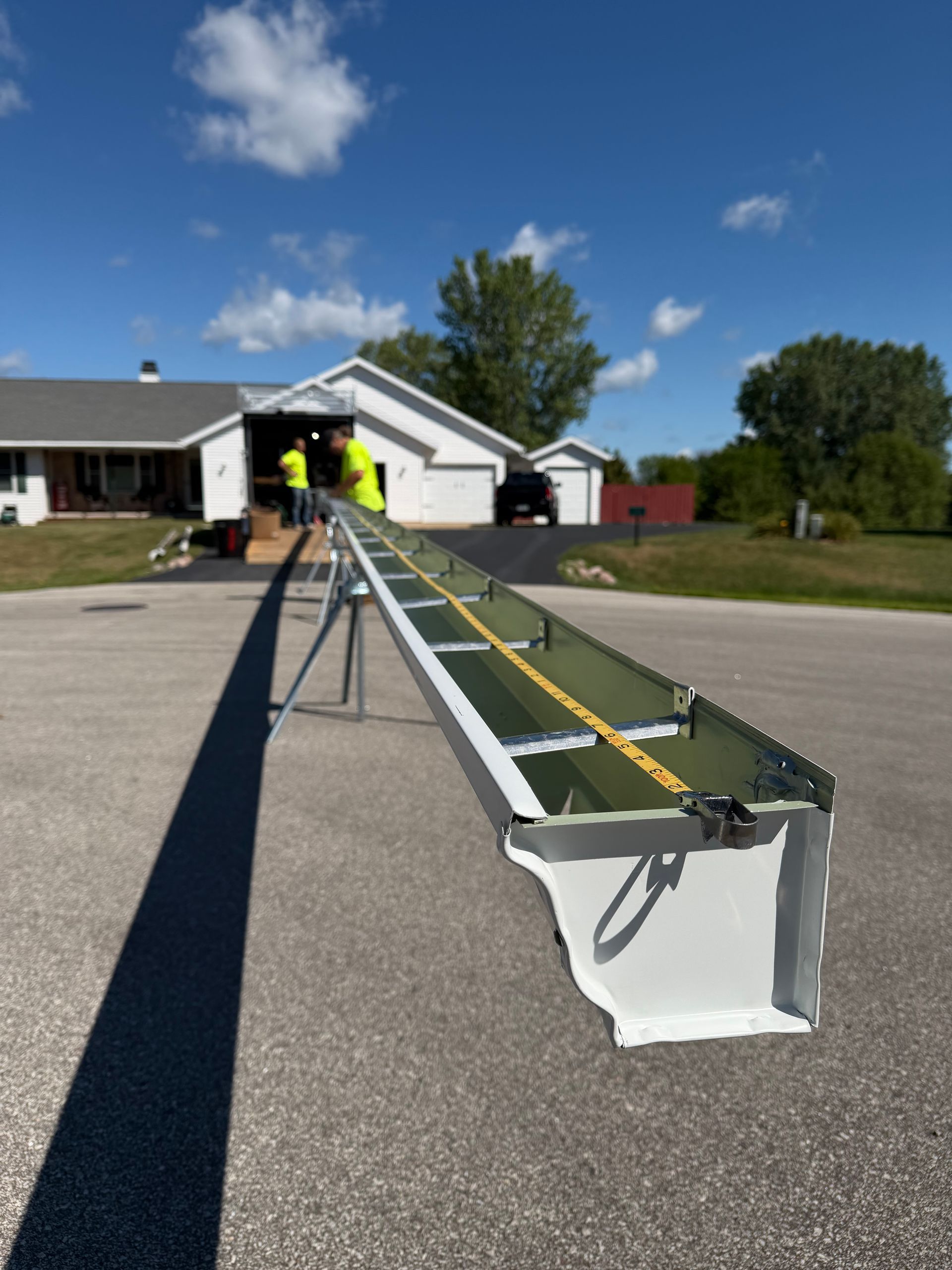 Long metal beam on driveway with workers near a house under a blue sky