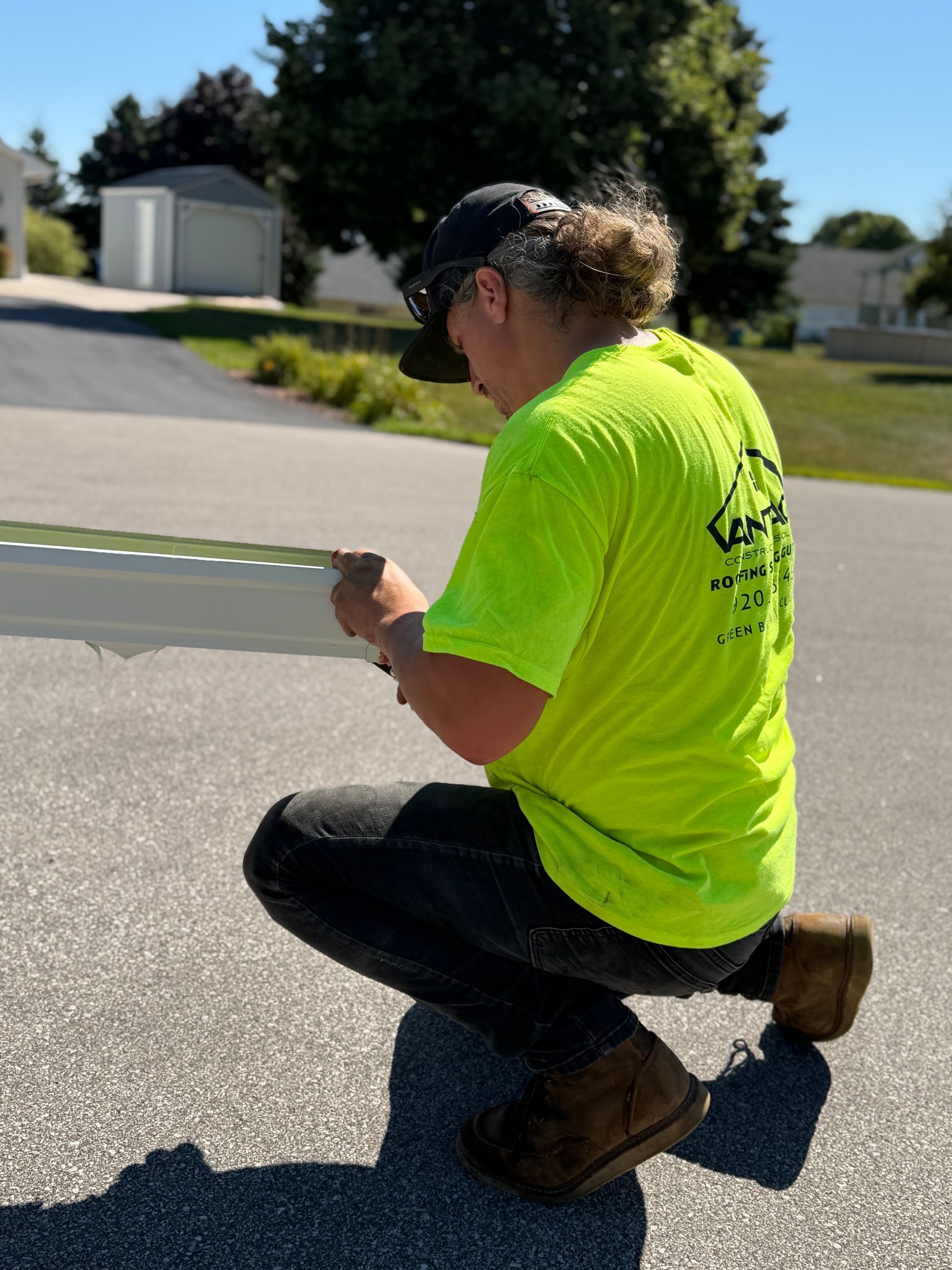 Worker in neon yellow shirt kneeling on pavement, measuring or inspecting something outdoors.