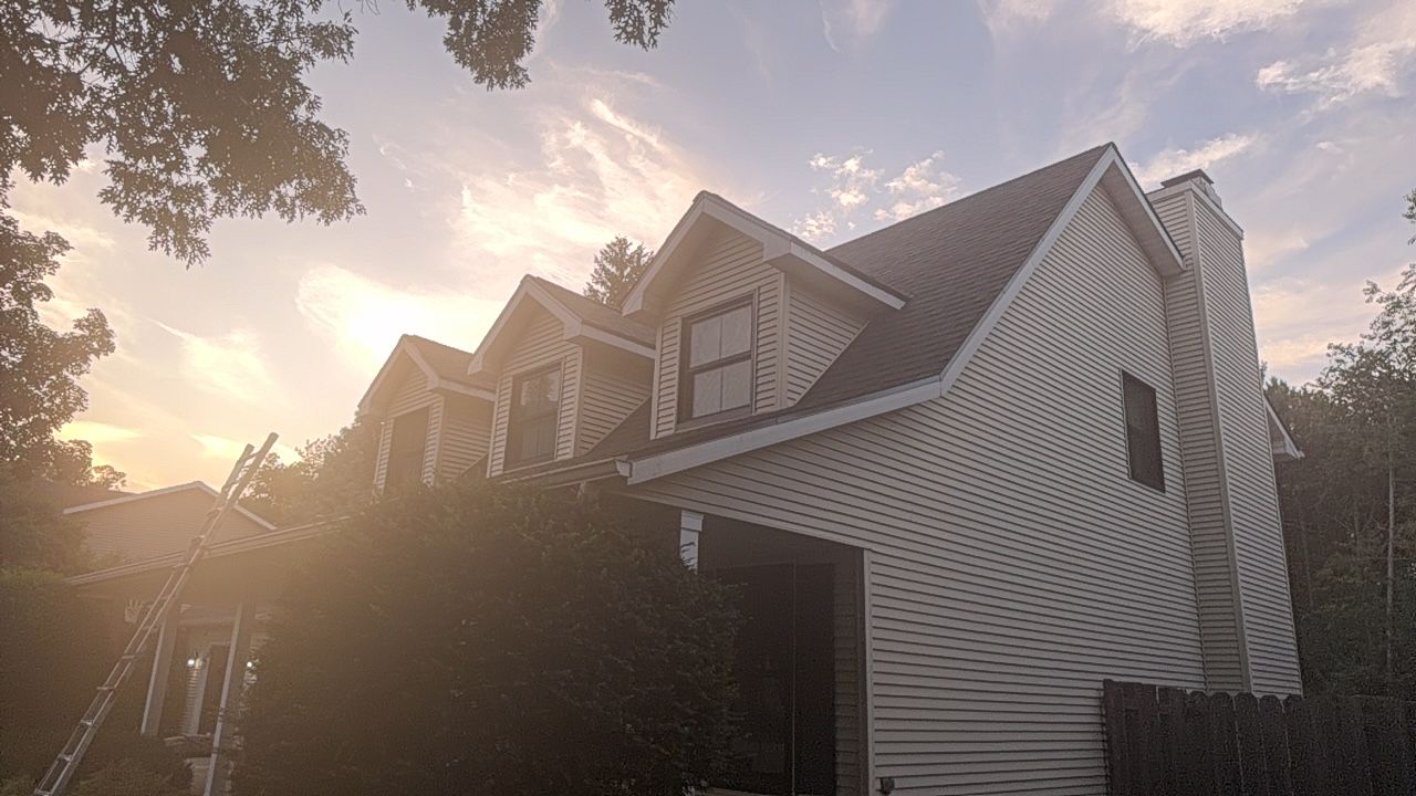 Sunlit white house with dormer windows and dark roof, seen through trees at sunset