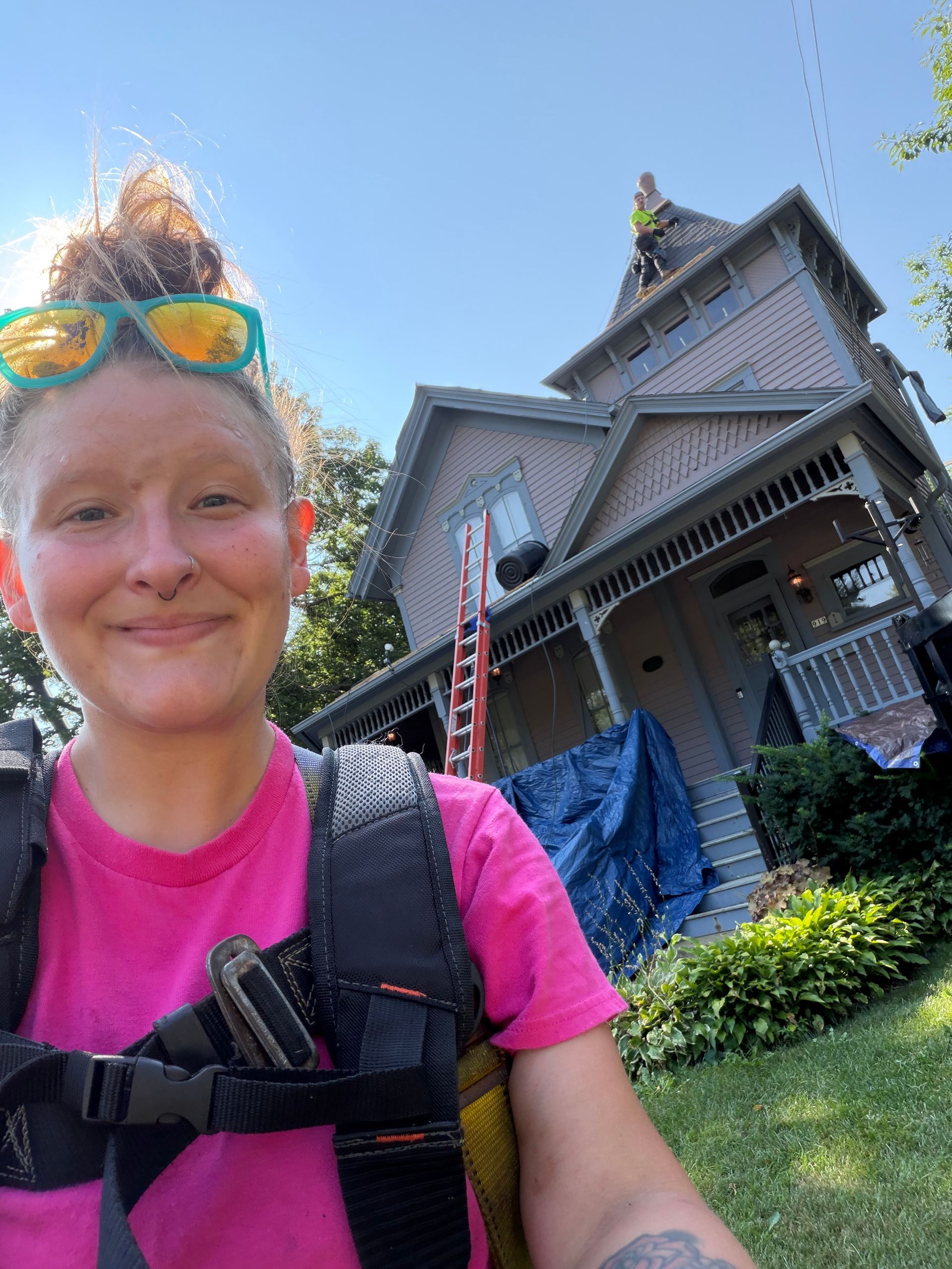 Smiling hiker in pink shirt with backpack in front of a Victorian house on a sunny day