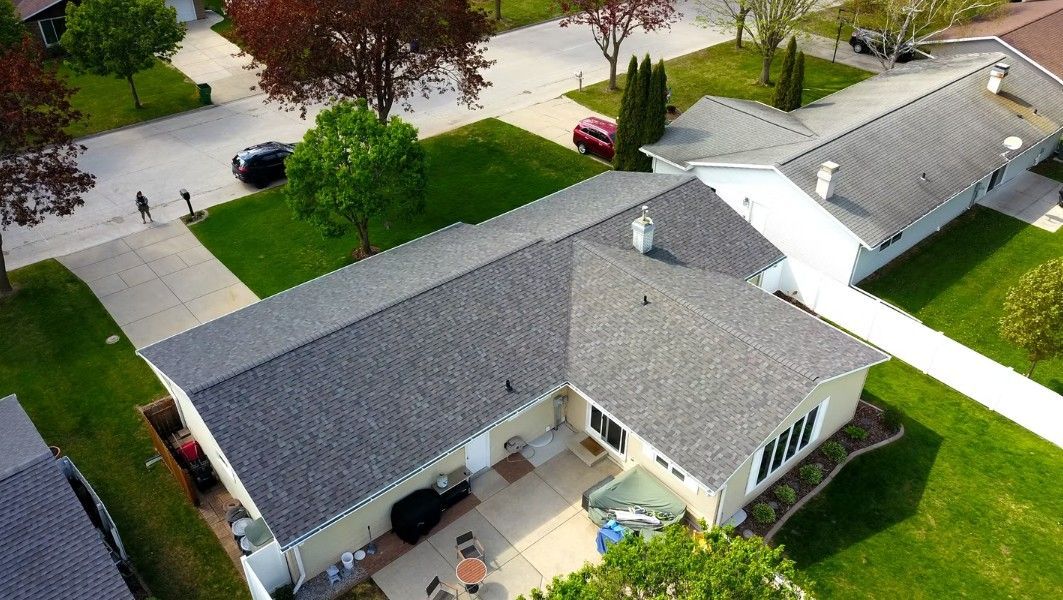 Aerial view of a suburban house with gray roof, green lawn, and driveway.