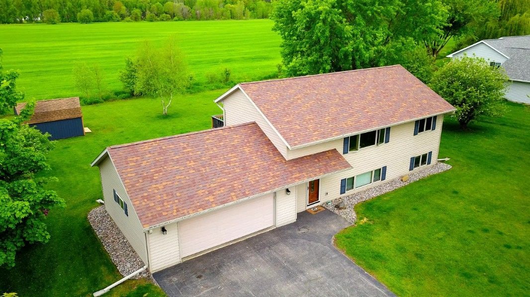 Aerial view of a beige two-story house with a red roof, garage, driveway, and green lawn.