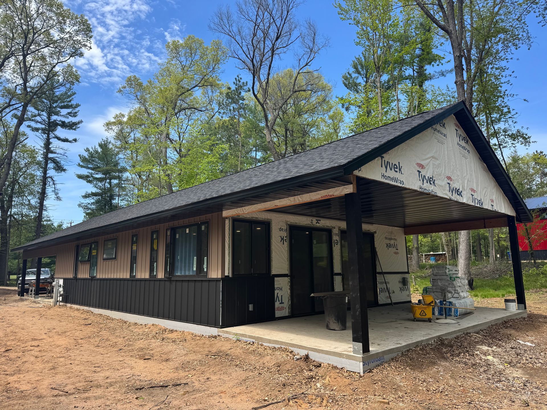 Small black cabin with a covered porch in a pine forest on a sunny day
