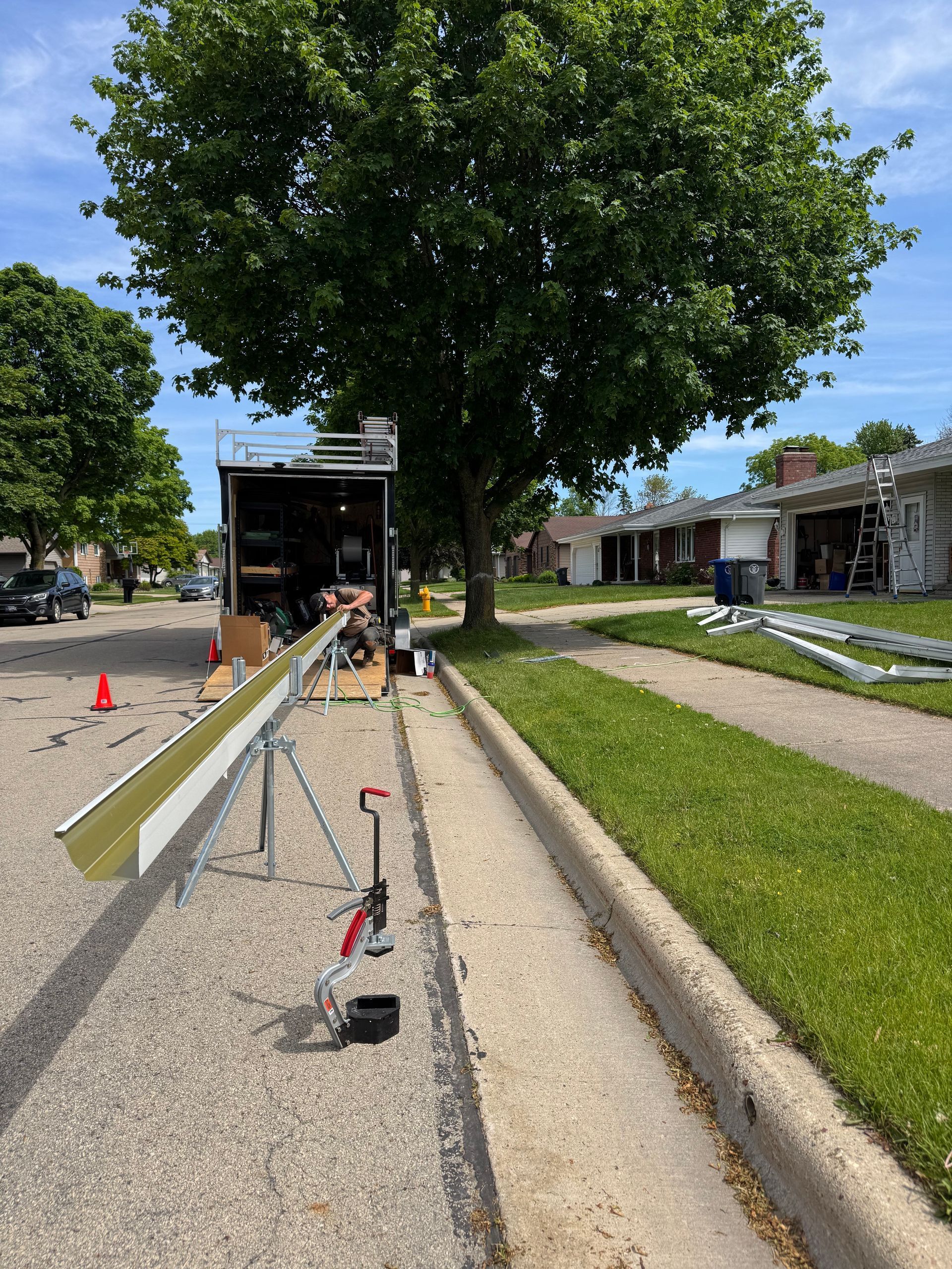 Utility workers repairing a sidewalk beside a large tree and parked truck on a sunny street