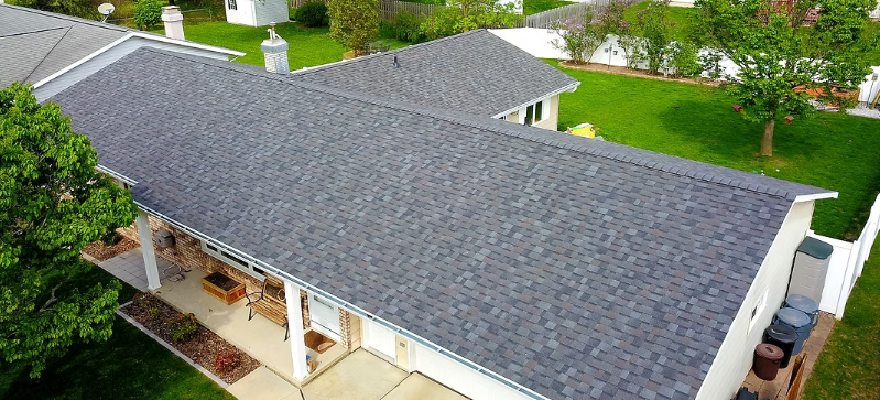 Aerial view of a house with a gray shingle roof and white trim in a green suburban neighborhood