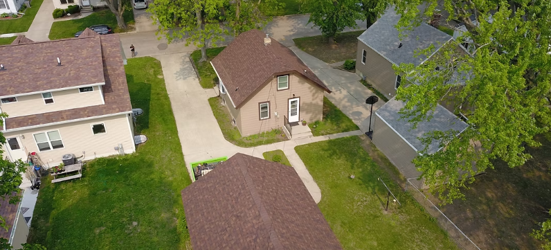 Aerial view of a large gray-roofed house beside a wooded lakeshore
