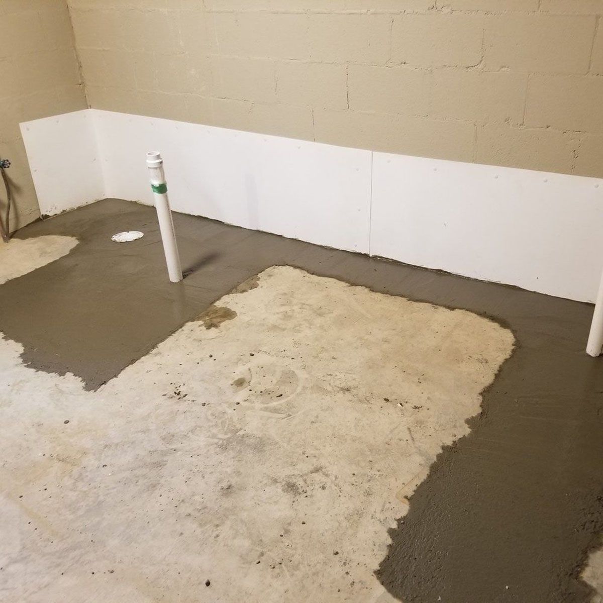 Bathroom floor with wet concrete, white wall panels, and exposed pipes under construction