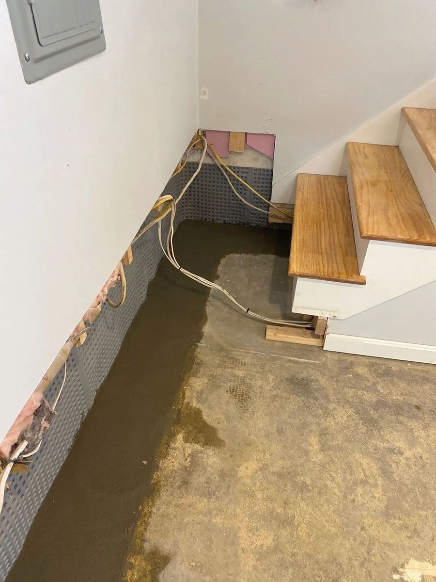 Basement stairwell with exposed wiring, damp concrete floor, and wooden steps