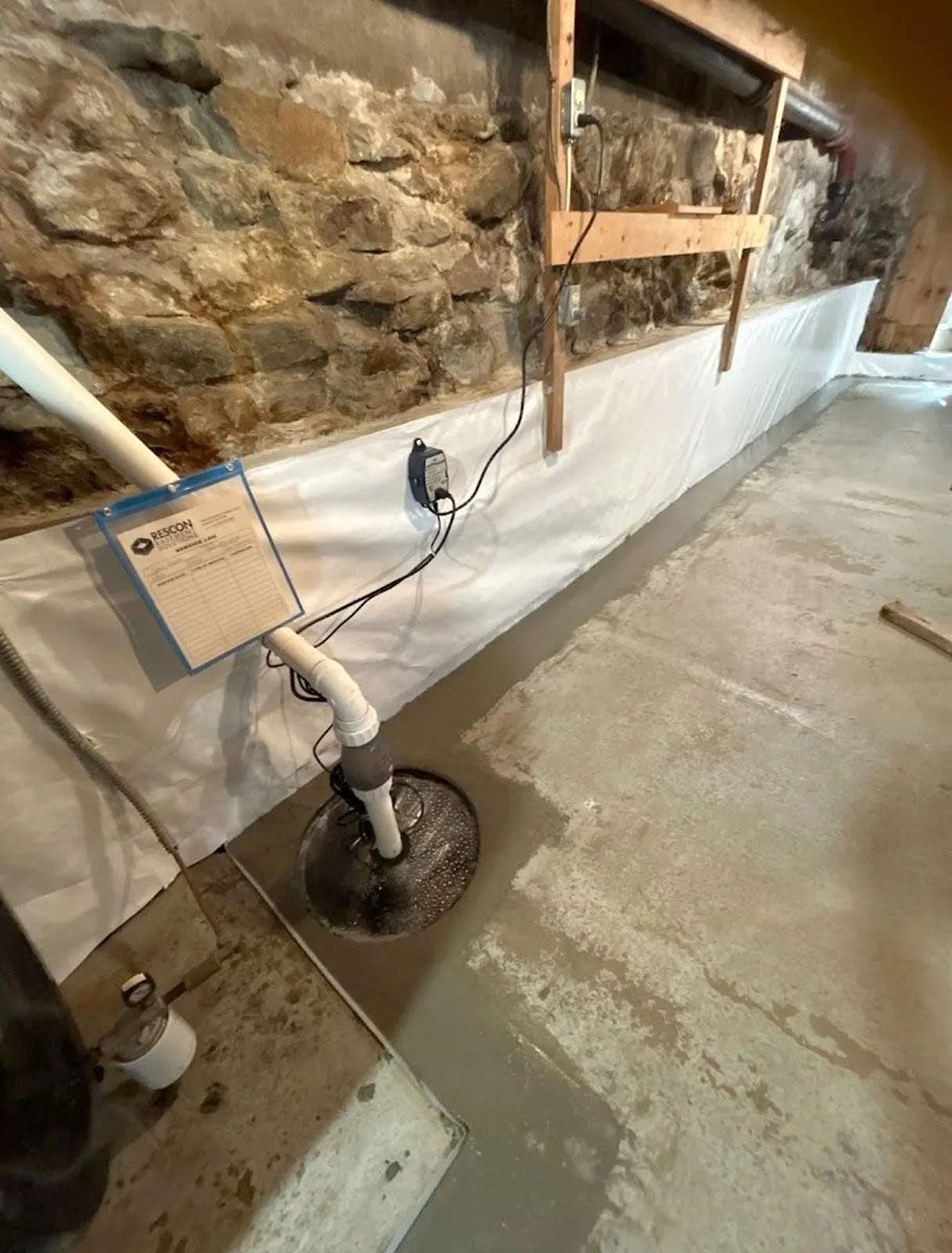 Plumbing pipe assembly on a basement floor beside a stone wall
