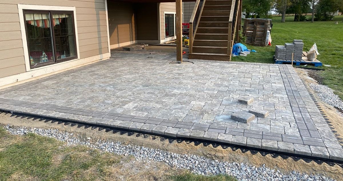 Patio with gray pavers, bordering, and stairs leading up. Partially completed with materials visible.