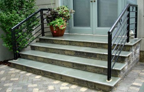 Stone steps with black metal handrails leading to glass double doors.
