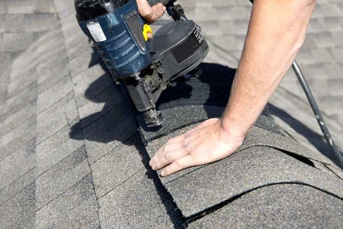 Person using a pneumatic nail gun to attach asphalt shingles to a roof.