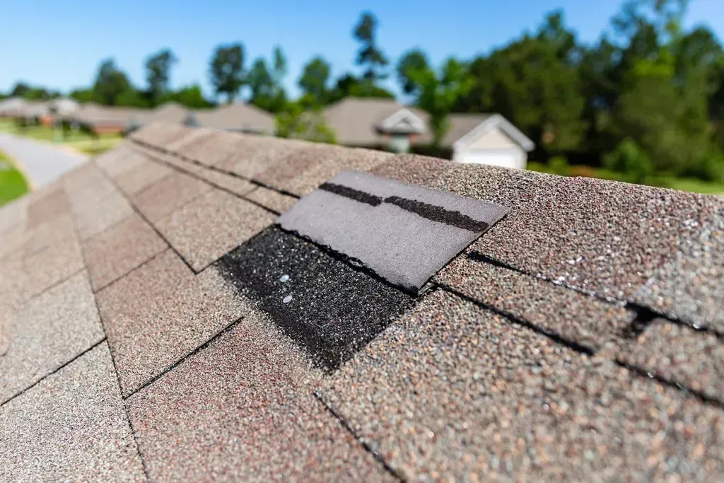 Close-up of a damaged asphalt shingle roof. The shingles are missing and dark in color.