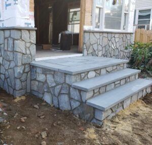 Stone steps and porch with gray stone facing; unfinished house entrance.