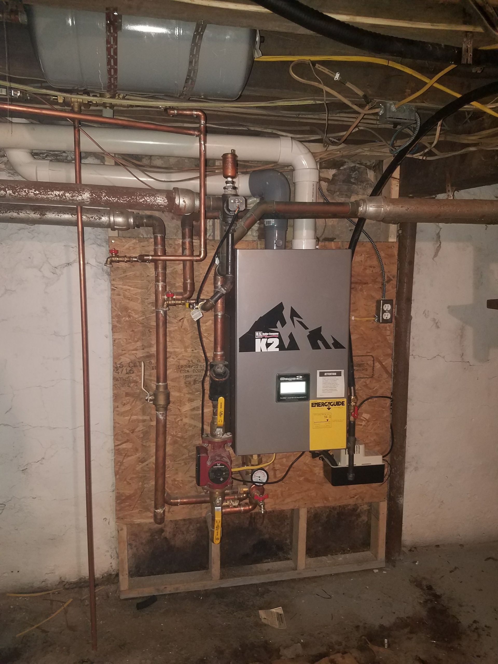 A boiler is installed in a basement with copper pipes.