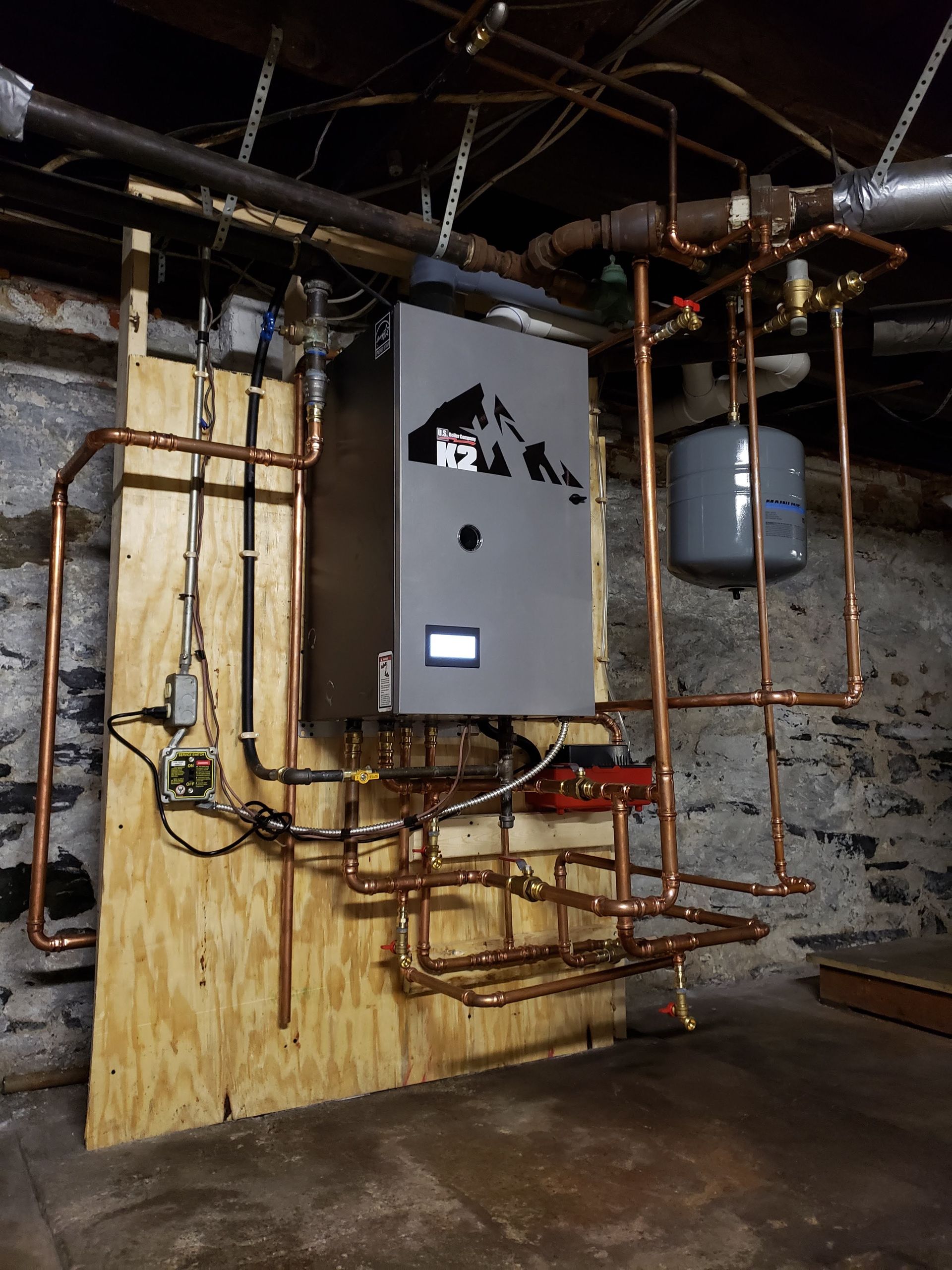 A boiler is installed in a basement with copper pipes.