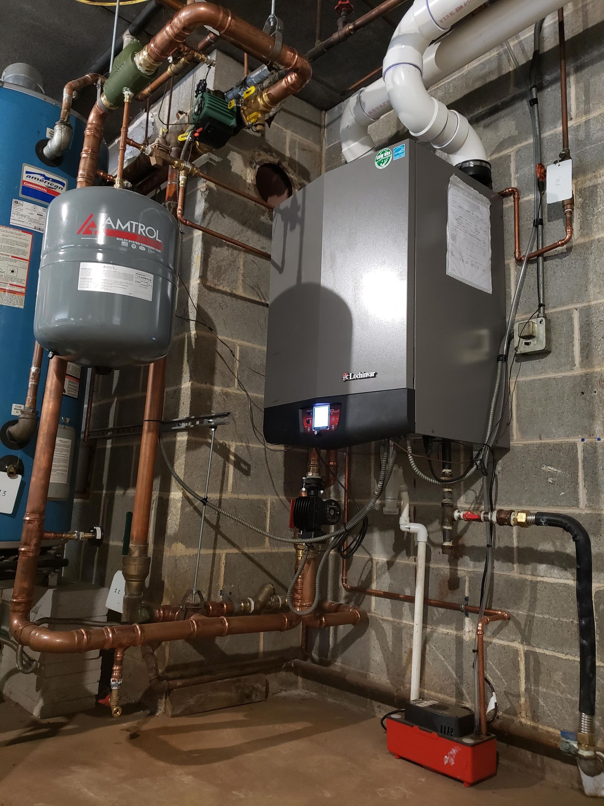 A boiler is sitting in a basement surrounded by pipes.