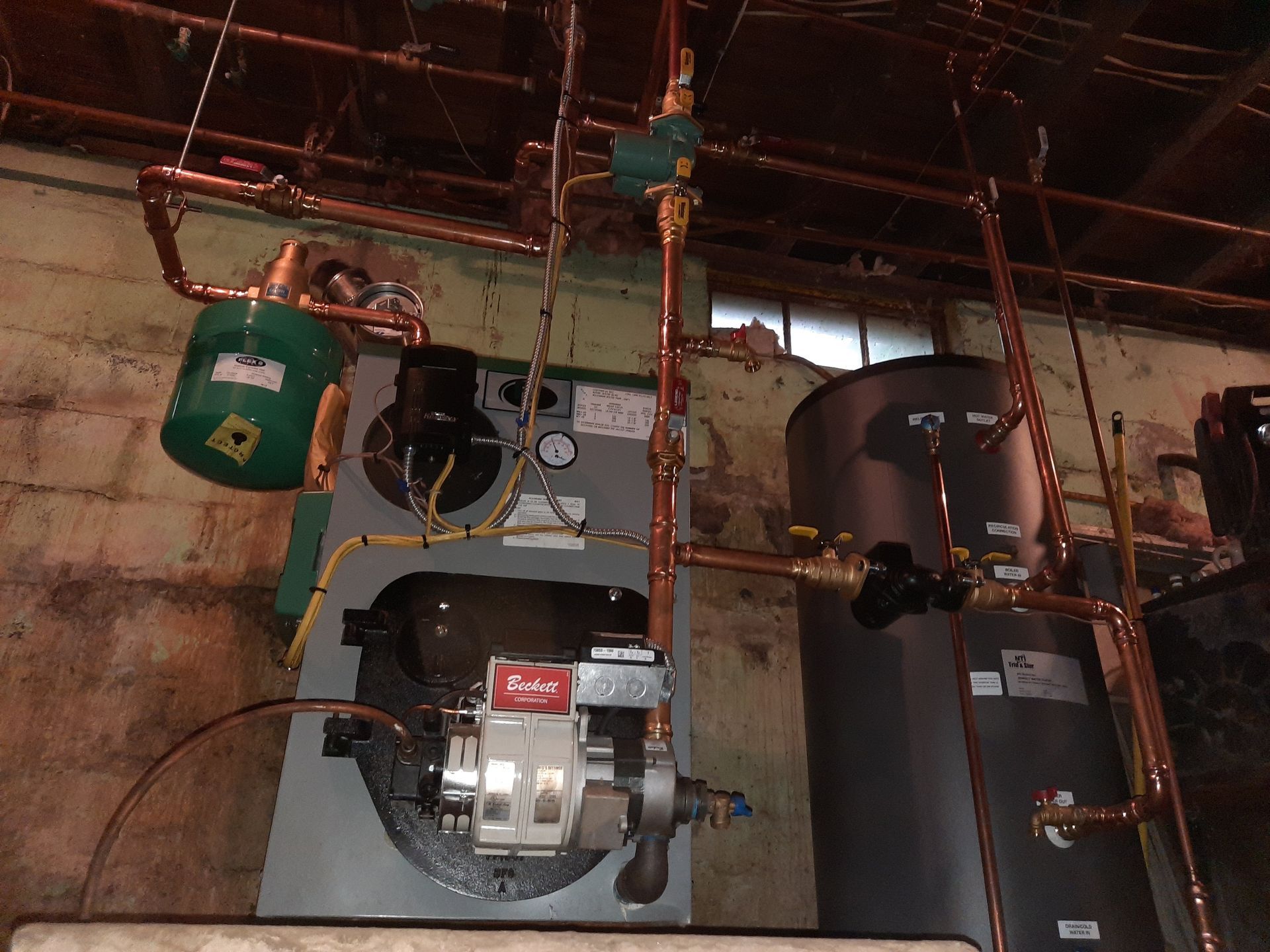 A boiler with copper pipes hanging from the ceiling.