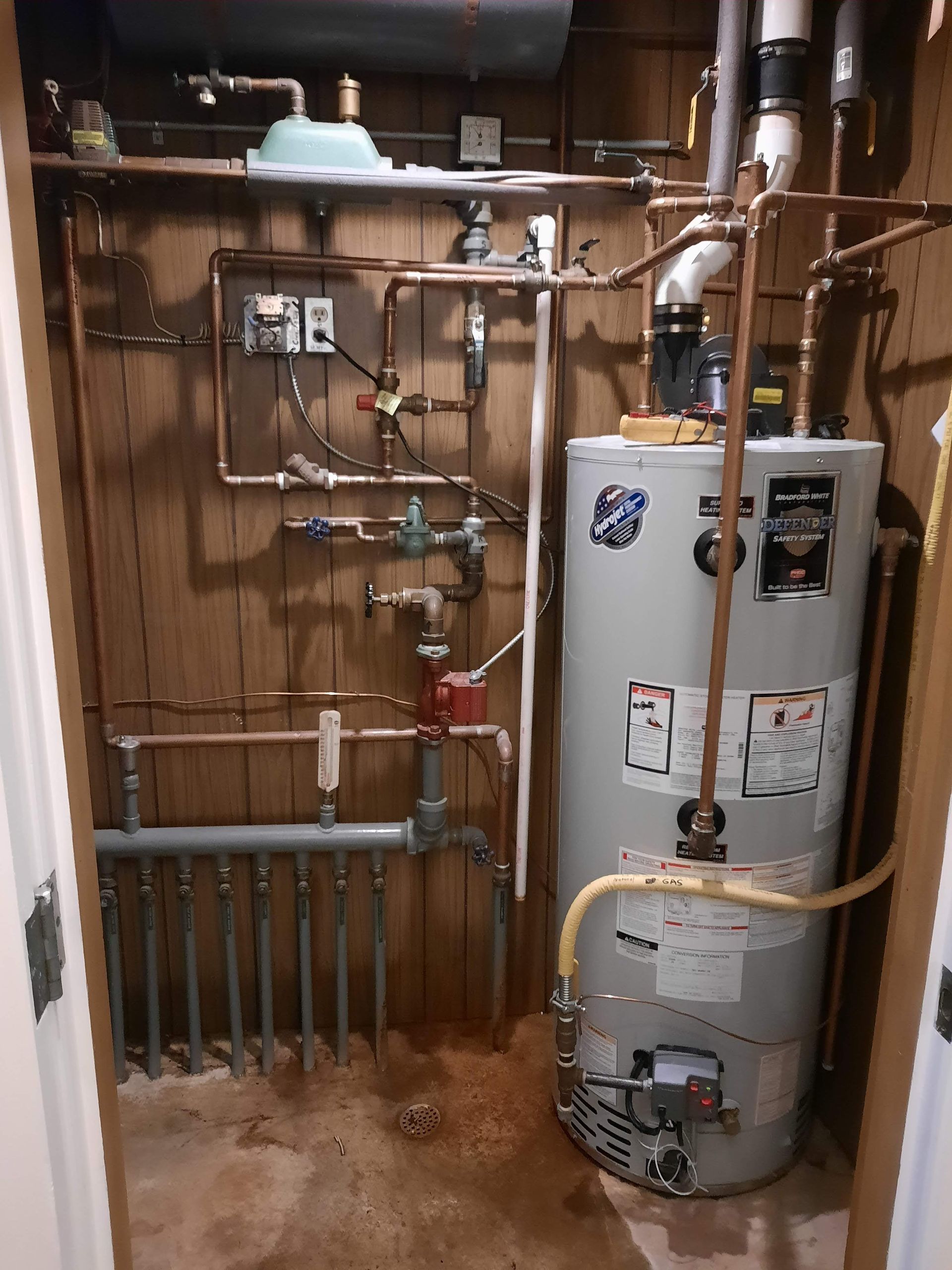 A room with a water heater and pipes on the wall.