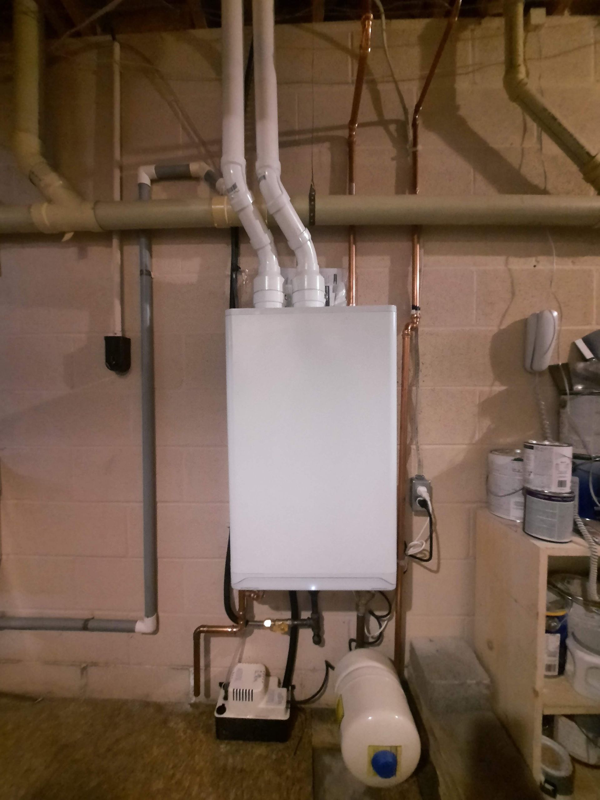 A white boiler is sitting in a basement with pipes coming out of it.