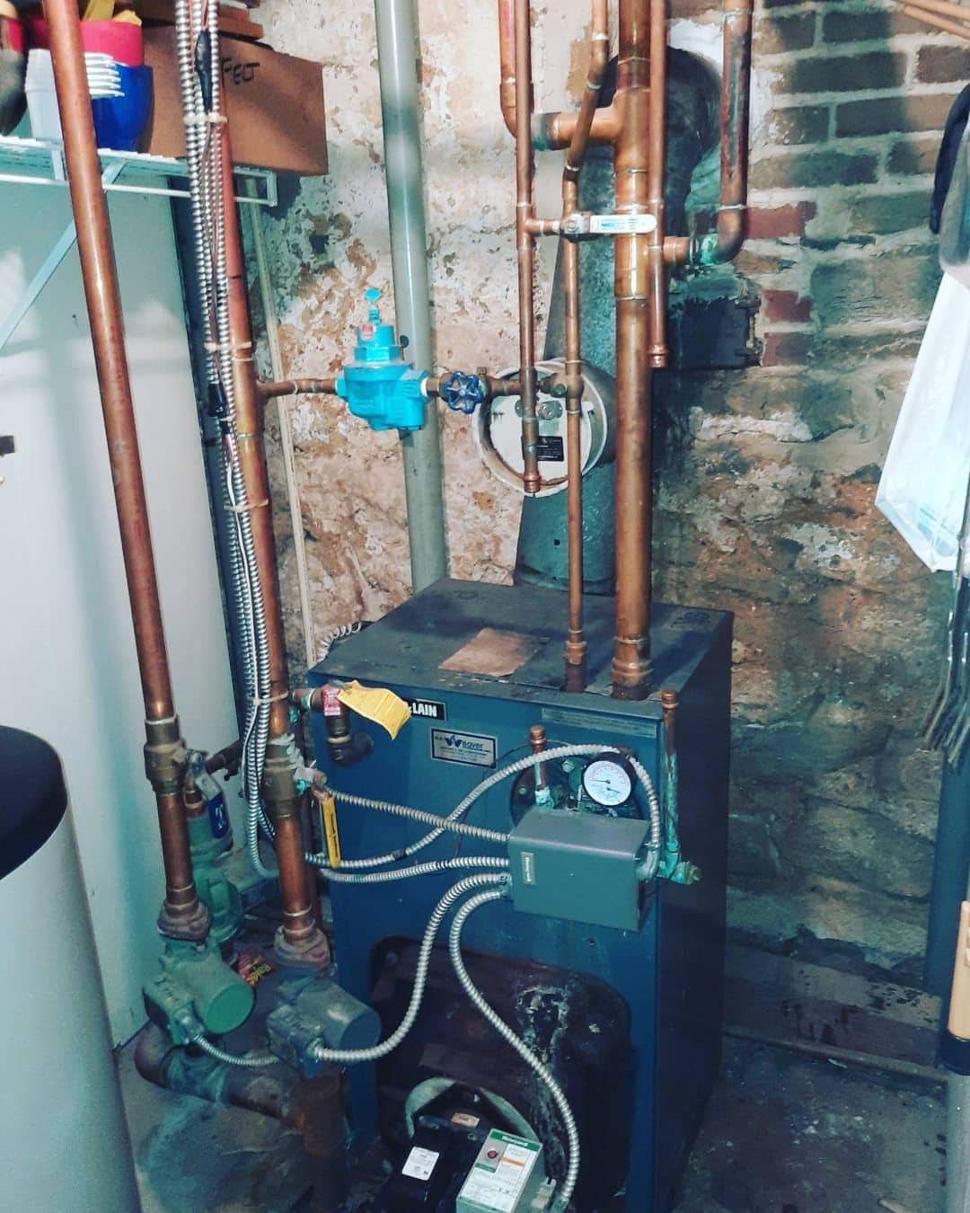 A boiler is sitting in a basement next to a brick wall.