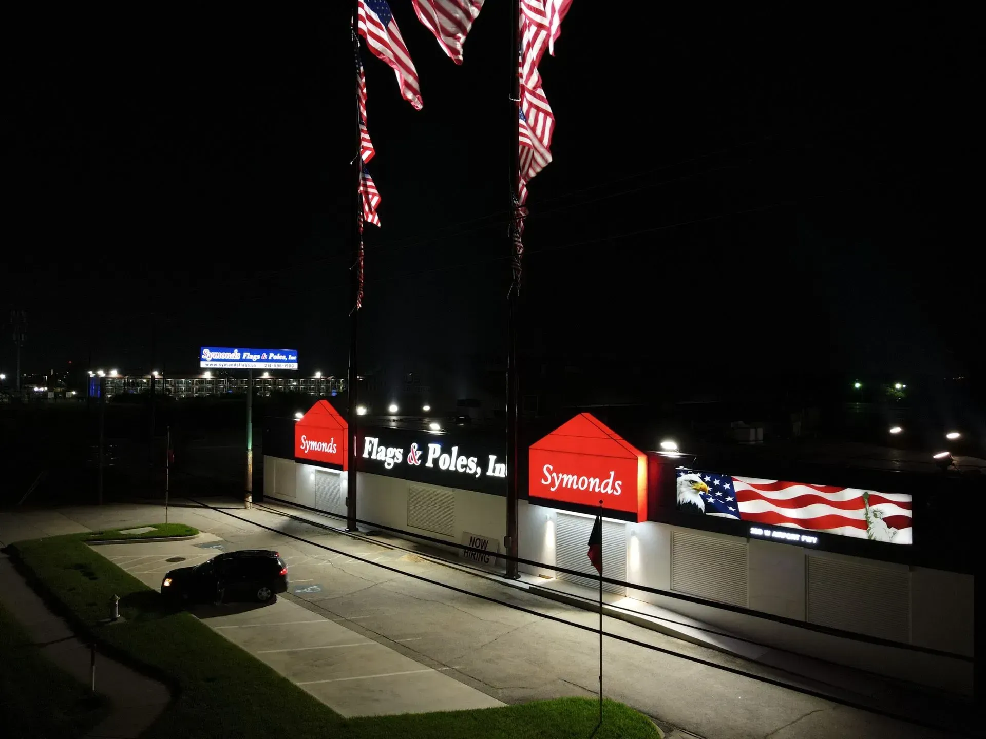 Night exterior shot of a building with US flags flying. Sign reads 