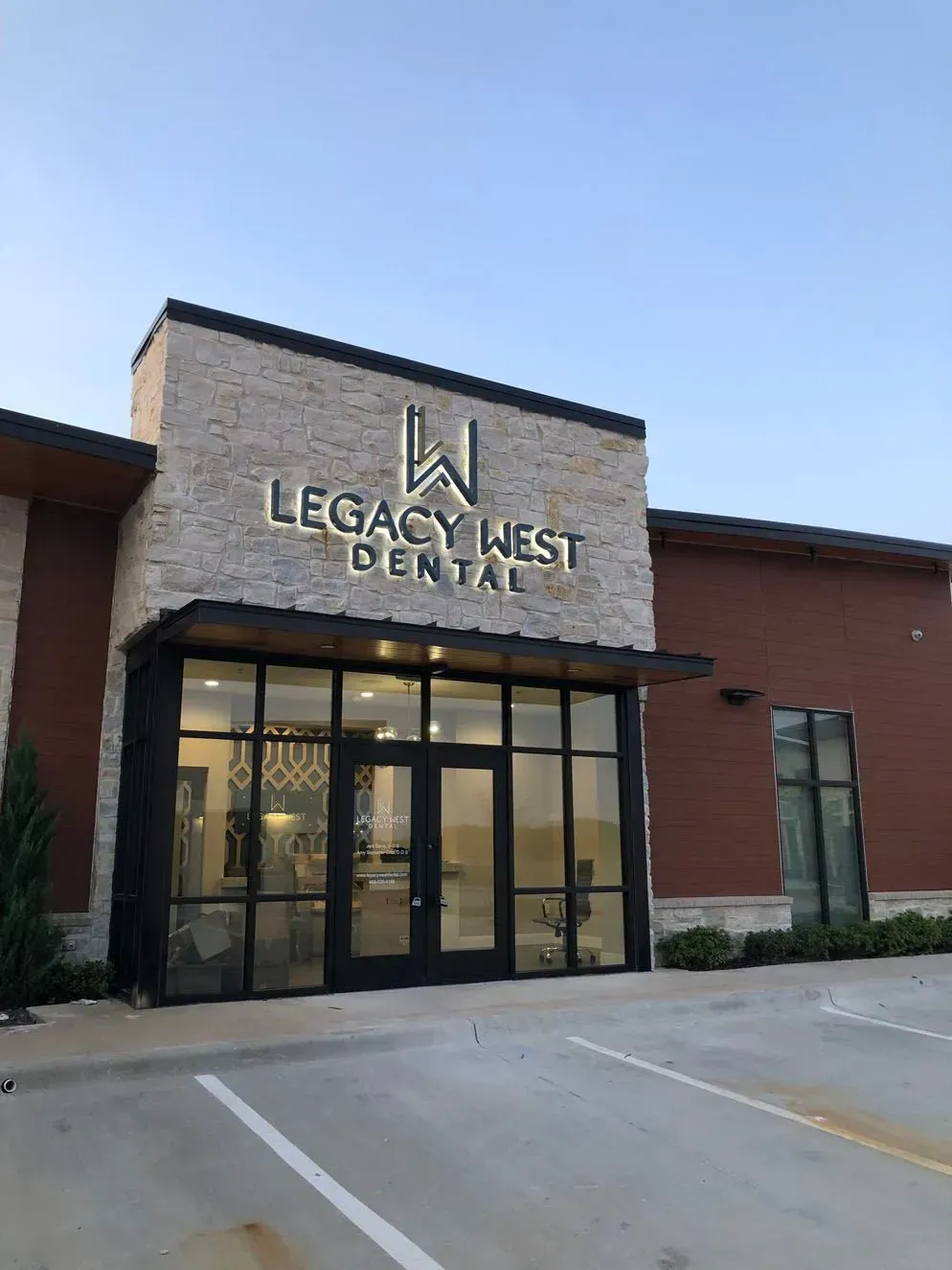 Exterior of Legacy West Dental building with illuminated sign and glass doors.