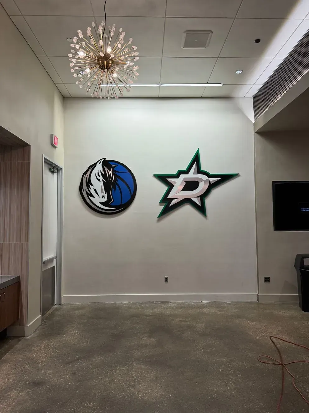 Mavs and Stars logos on a wall in a room with a concrete floor, and a chandelier.
