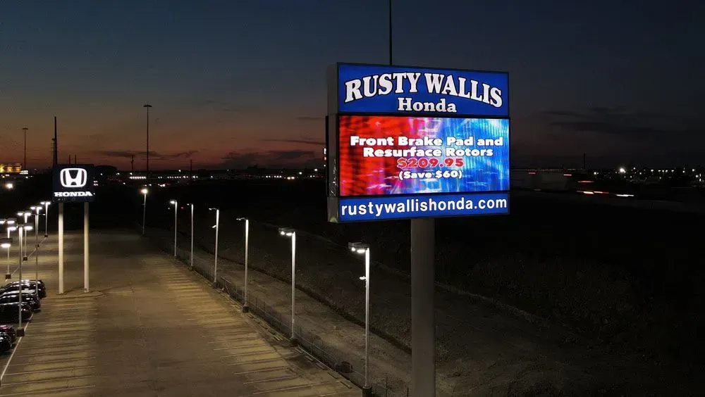 Night view of Rusty Wallis Honda dealership sign, advertising front brake pad and resurface rotors service.