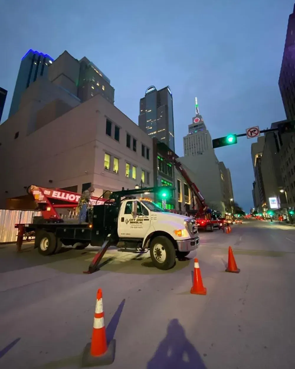 White utility truck with an extended arm working on a building facade in a city street at dusk.