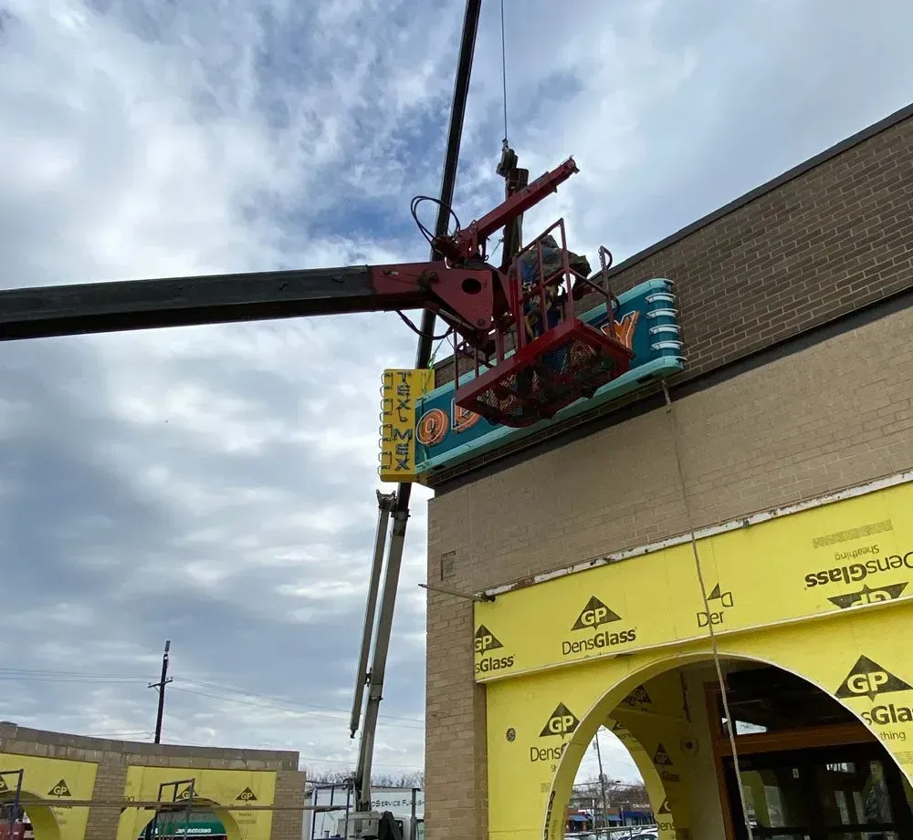 Sign being removed from a building by a lift. Construction zone, cloudy sky.