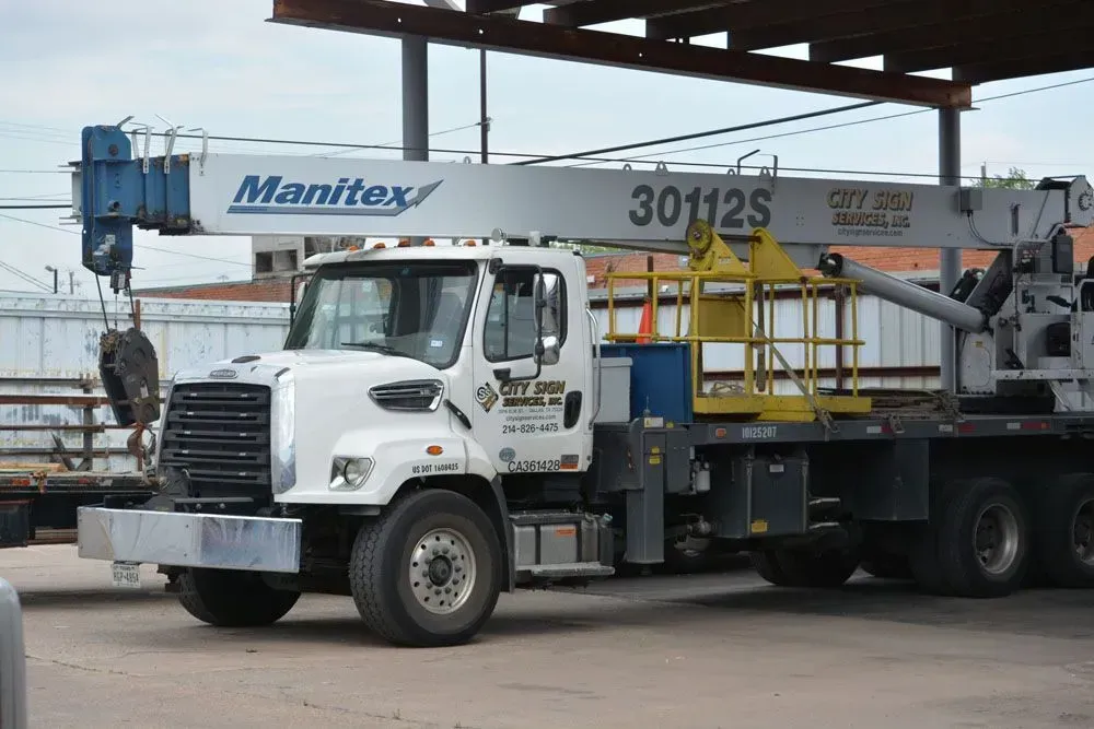 White Manitex crane truck parked under a metal structure.