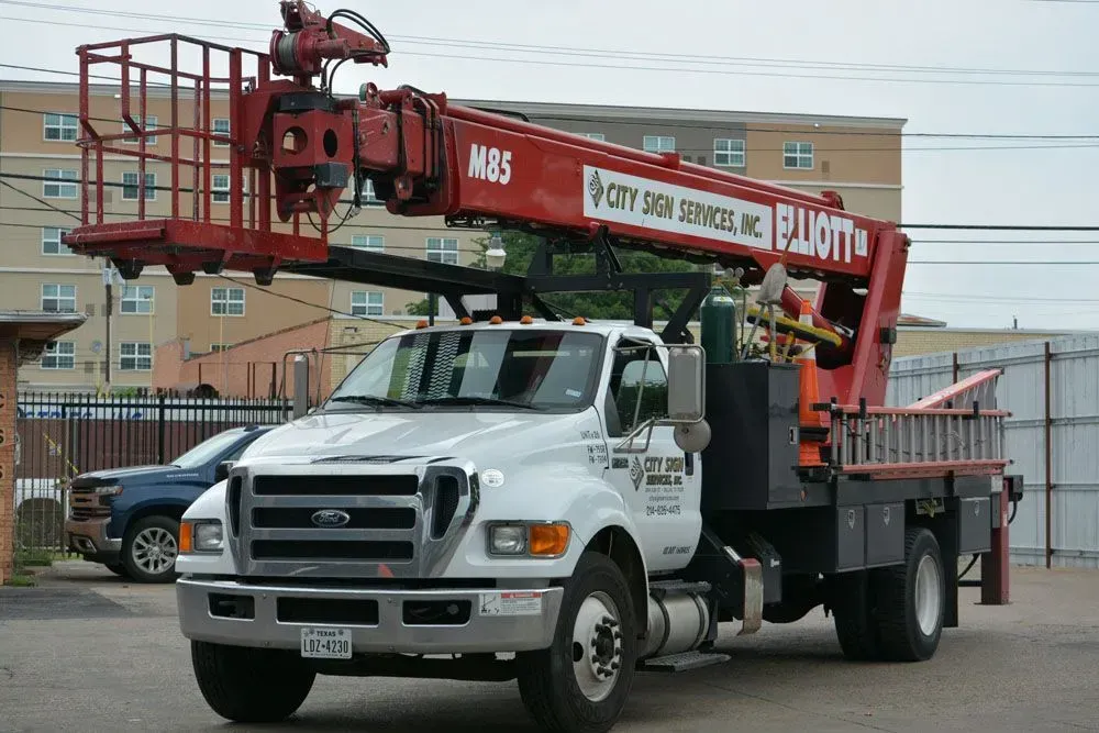 White truck with red aerial lift for sign services. Building in the background.