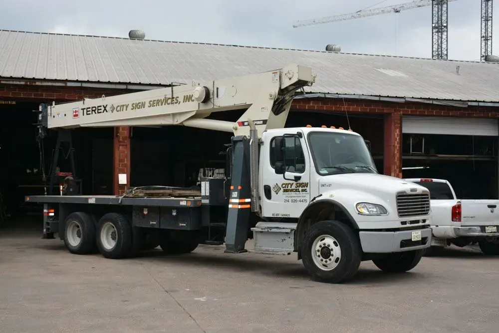 White flatbed truck with crane in front of brick building.