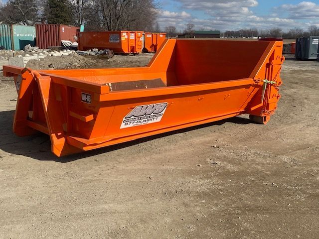 A large orange dumpster is parked in a dirt lot.