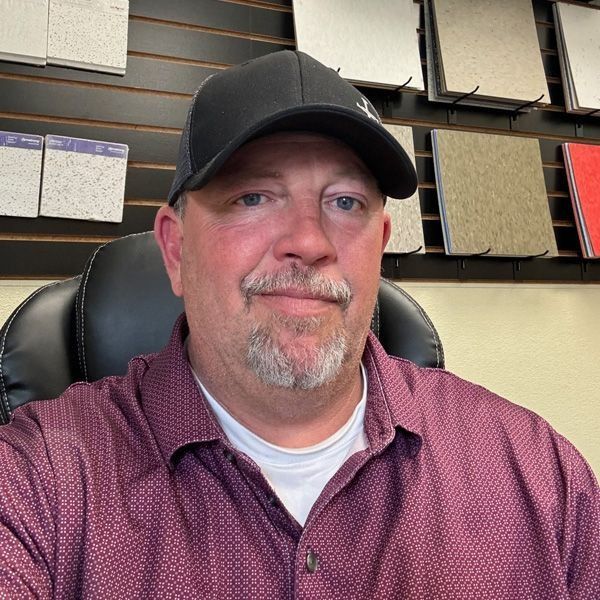 Man in a black cap and maroon shirt sitting in an office, looking at the camera with a slight smile.