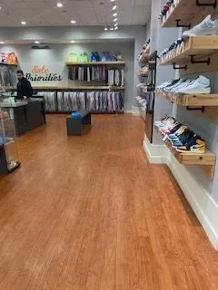 Empty shoe store interior with wood floors, shelves, and clothing racks along the back wall