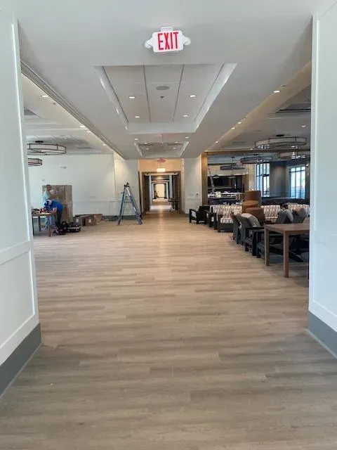 Bright hallway in a modern building with wood floors, chairs along the wall, and an exit sign overhead