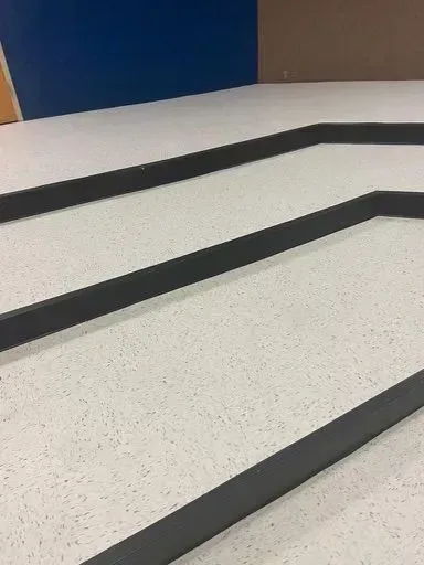 Black stair treads on a light speckled floor beside a blue wall.