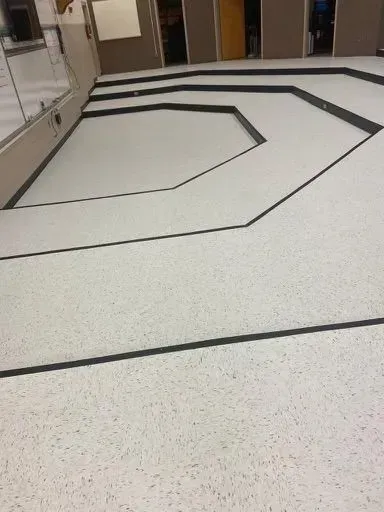 White speckled floor with black geometric lines in a hallway or lobby area.